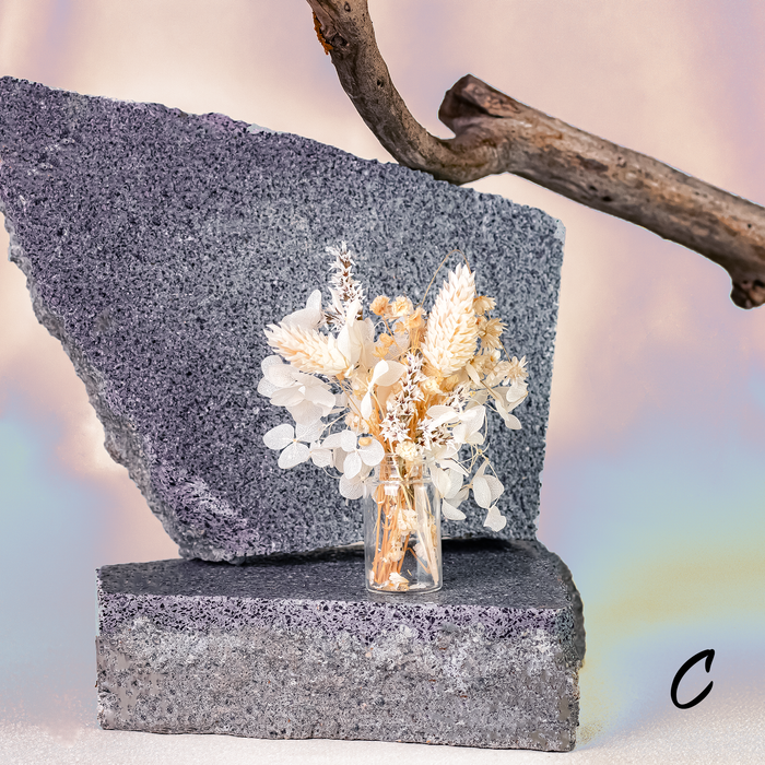 Mini bouquet of dried flowers in delicate glass vase displayed on a rock.