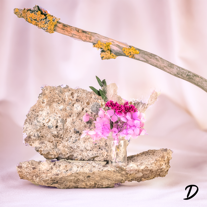 Mini bouquets of dried rose, pink, and green  flowers in delicate glass vase displayed on a rock.