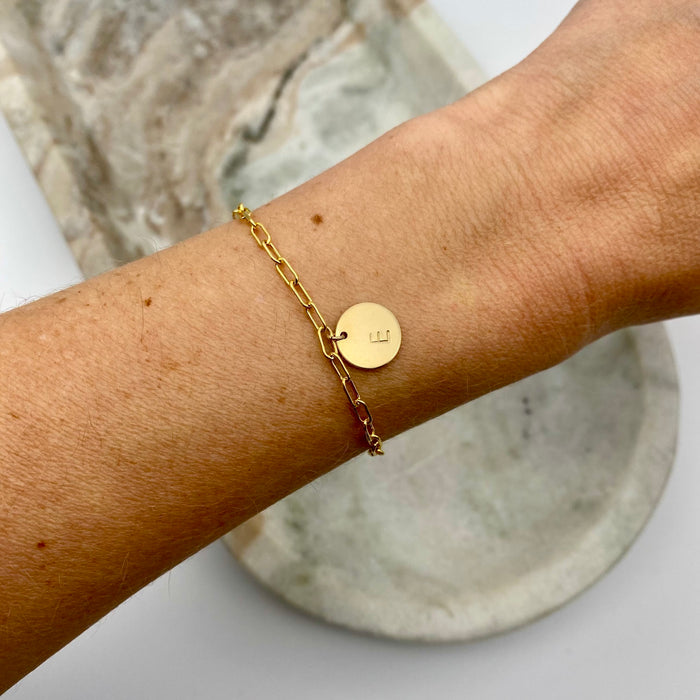This bracelet features a 14-karat gold-filled paperclip chain, complemented by one gold-filled coin charm. The charm is personalized and distinctively stamped with one letter.