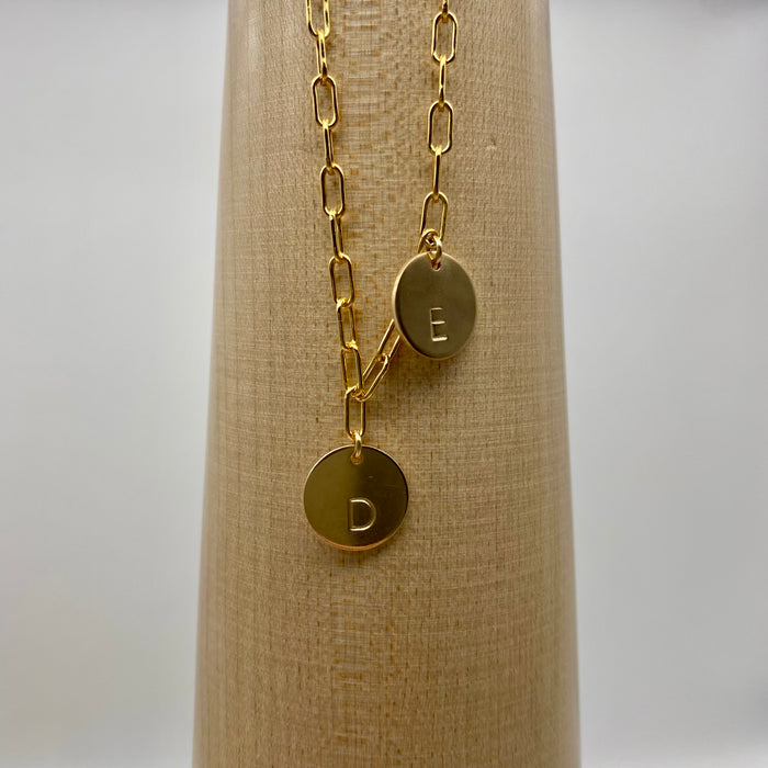 Close up of a 14-karat gold-filled paperclip chain, complemented by two gold-filled coin charms. Each charm is personalized and distinctively stamped with one letter.