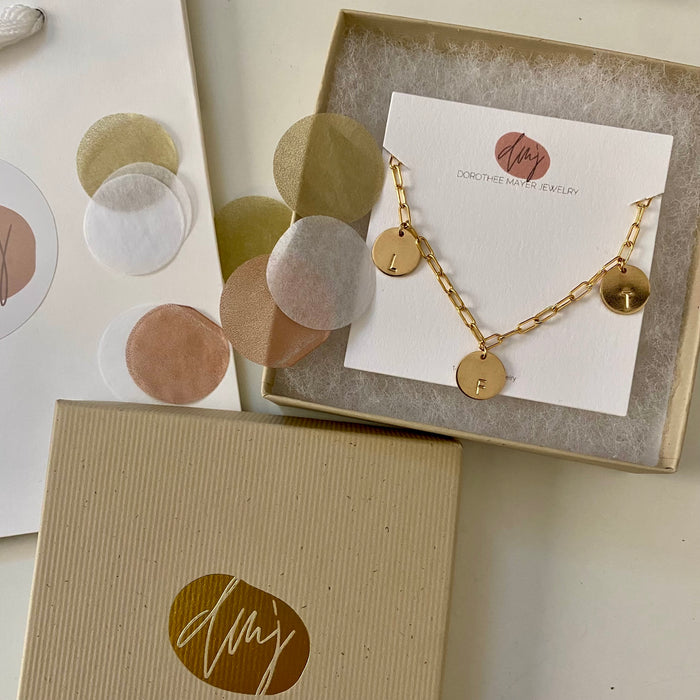 This bracelet features a 14-karat gold-filled paperclip chain, complemented by two gold-filled coin charms. Each charm is personalized and distinctively stamped with one letter.