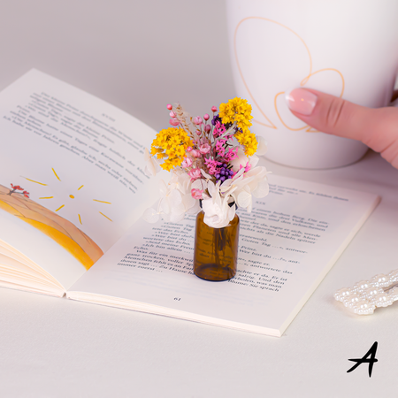 Mini bouquet of dried flowers in delicate glass vase howcase in a home setting on an opened book page.