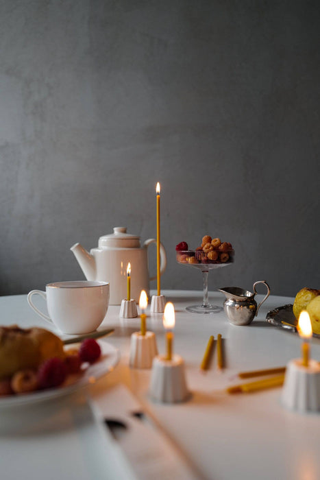 Thin and fine candle in five porclein canlde holders on a table set for afternoon coffee.