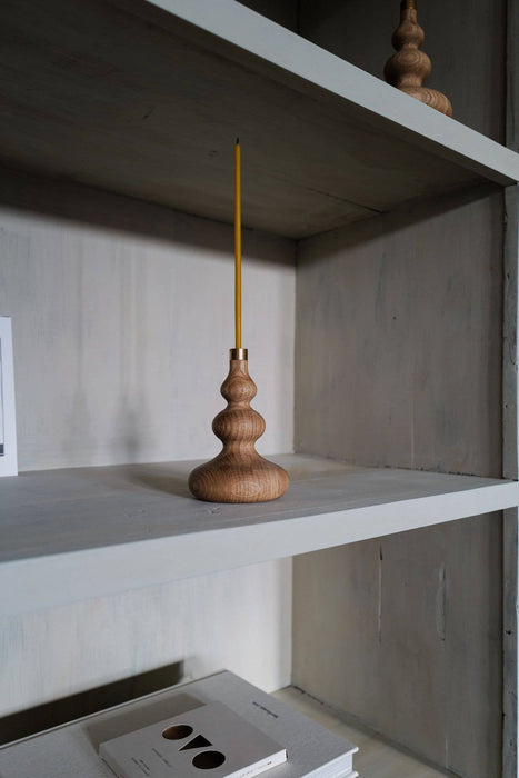 Oiled oak candle stick holder with brass detail and beeswaxed candle on a shelf.