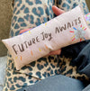 Small pillow with 'Future Joy Awaits' text held by a person wearing a leopard print garment.