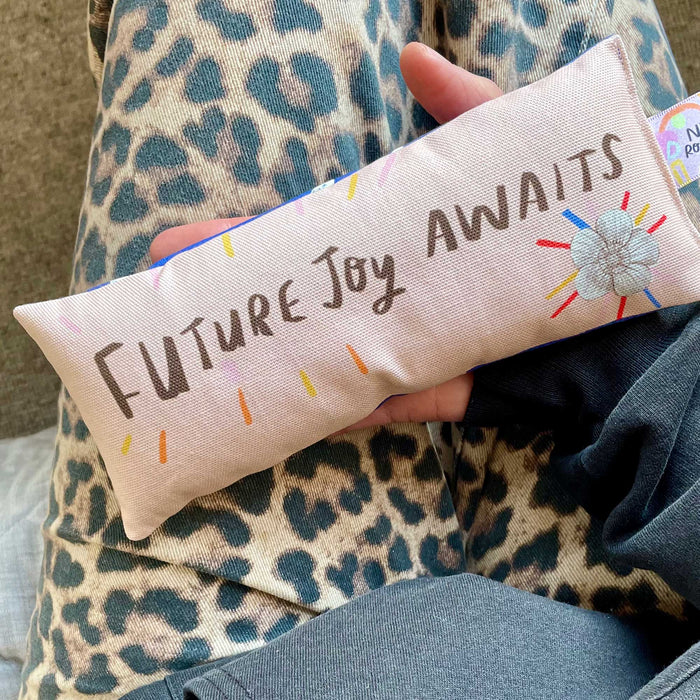 Small pillow with 'Future Joy Awaits' text held by a person wearing a leopard print garment.