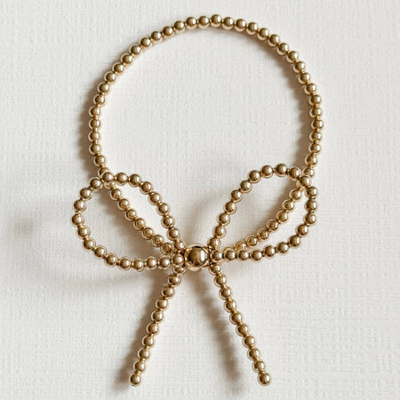 A gold filled bracelet with a bow detail, double strung on elastic, displayed against a neutral background.