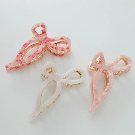 Three ribbon metal bow claw clips in pink, white, and red colors with a gold metal base.