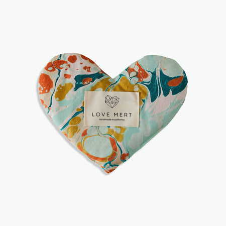 A heart-shaped 'Eye Love Pillow' with a marbled pattern of blues and pinks and the brand label 'LOVE MERT' attached to it.