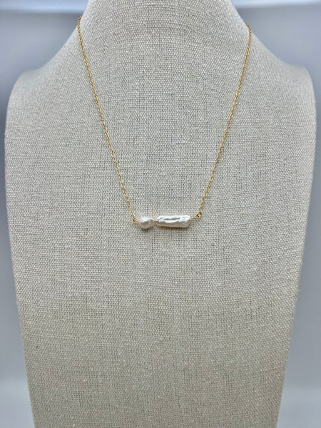 A gold-colored necklace with a bar-shaped freshwater pearl pendant, displayed on a mannequin torso.