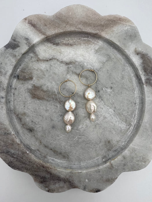 A pair of round freshwater pearl earrings with gold-filled metal hoops, displayed on a marble surface.
