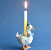 A porcelain goose cake topper with a blue bowtie and a blue hat, standing on a gold steel chain with a lit candle on top.