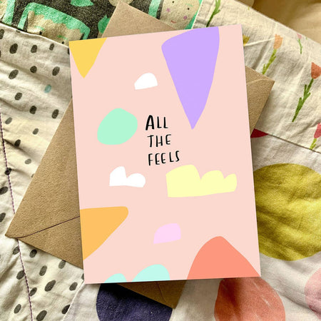 Card with colorful abstract shapes and 'All The Feels' text on a patterned fabric background