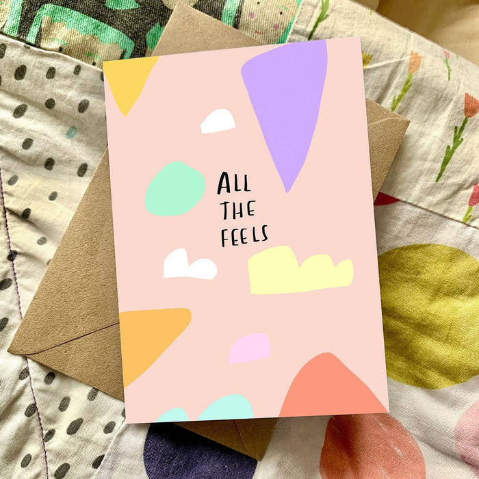 Card with colorful abstract shapes and 'All The Feels' text on a patterned fabric background