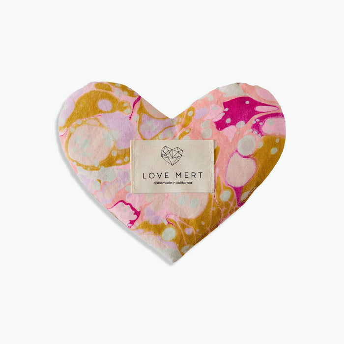 A heart-shaped 'Eye Love Pillow' with a marbled pattern of pink and yellow tones on a white background and a label that reads 'LOVE MERT'.
