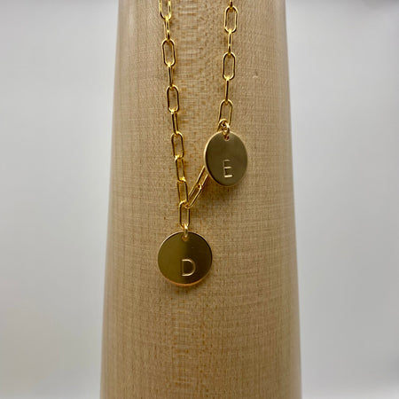 Close up of a 14-karat gold-filled paperclip chain, complemented by two gold-filled coin charms. Each charm is personalized and distinctively stamped with one letter. 