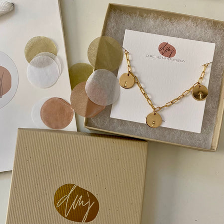 This bracelet features a 14-karat gold-filled paperclip chain, complemented by two gold-filled coin charms. Each charm is personalized and distinctively stamped with one letter. 