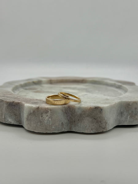 A single gold ring with a straight line texture design, displayed on a textured stone surface.