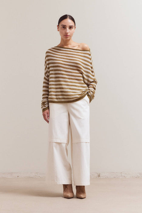 Woman wearing a striped sweater and white pants against a plain background