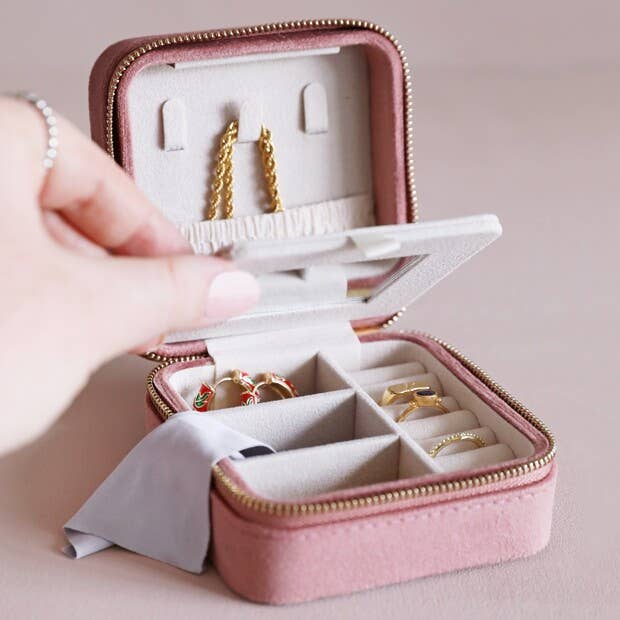 Open case with the inside half-filled with three small divider pockets, and a row of ring rolls for rings or earrings.  On the inside of the lid, a small square mirror is attached to make fastening your jewelery on the move even easier, and when a tab above the mirror is pulled down, a secret compartment with 3 necklace hooks and a pouch is hidden behind for more storage.