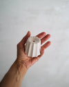 Candle holder in the shape of a traditional French dessert canelé in a matte white finish displayed n the palm of a hand.